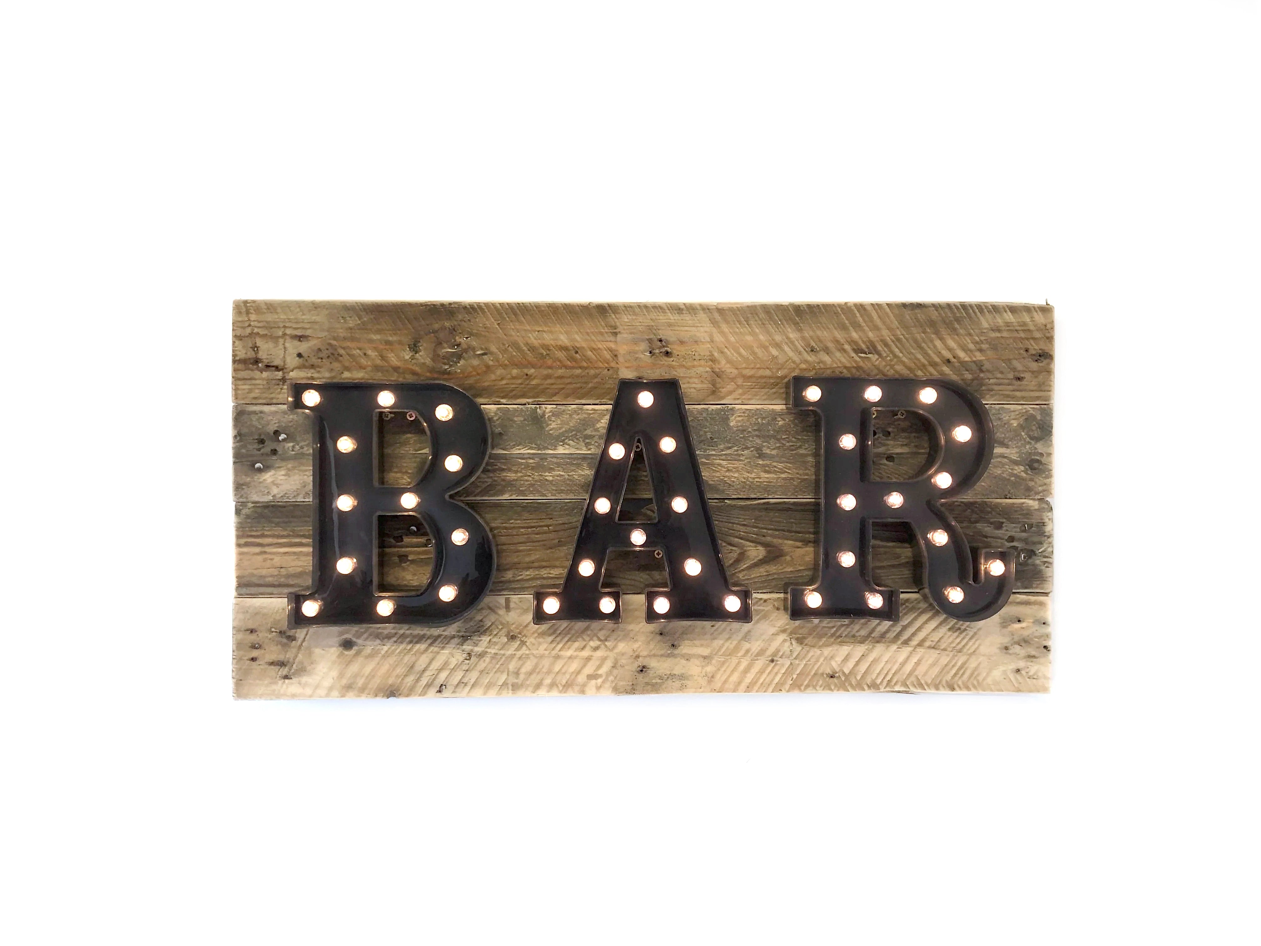 A rustic wooden sign featuring the word 'BAR' in large, black marquee-style letters with warm white light bulbs, mounted on a weathered brown wood plank background.